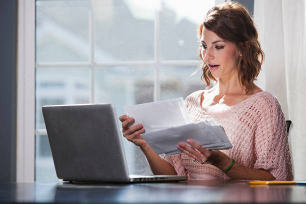 Paying bills Young woman (20s) with laptop, going through mail, paying bills. Sc0601 stock pictures, royalty-free photos & images