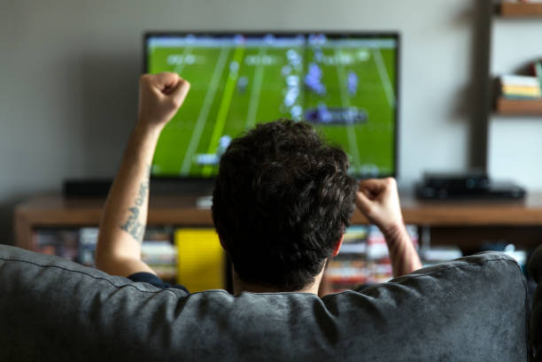 Man watching American football Man watching American football on tv and cheering keep an eye on stock pictures, royalty-free photos & images