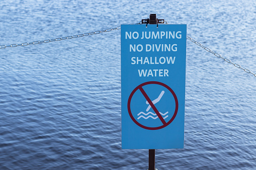 Sign no jumping, no diving from wooden pier, shallow water. Dangerous warning sign.
