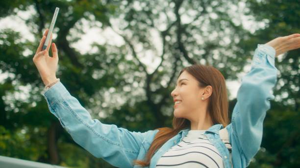 istock Cheerful Asian university student taking video call or selfie, walking under green trees on university park with happiness 1724639416