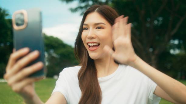 istock Cheerful Asian university student taking video call or selfie, walking under green trees on university park with happiness 1724640516