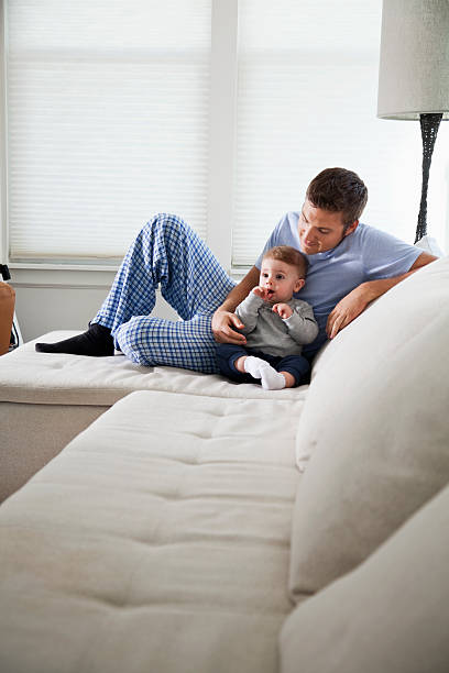 Father relaxing with baby Young father (20s) at home, sitting on couch with baby boy (8 months). Sc0601 stock pictures, royalty-free photos & images