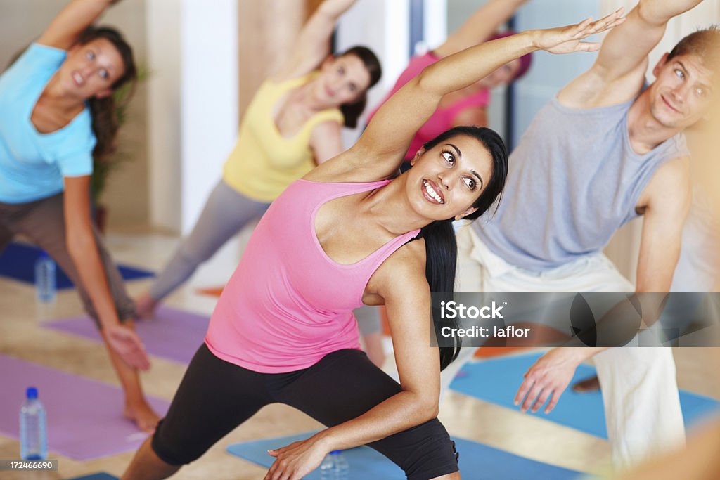 Stretching away to fitness Shot of an attractive young woman enjoying yoga class surrounded by other students Active Lifestyle Stock Photo