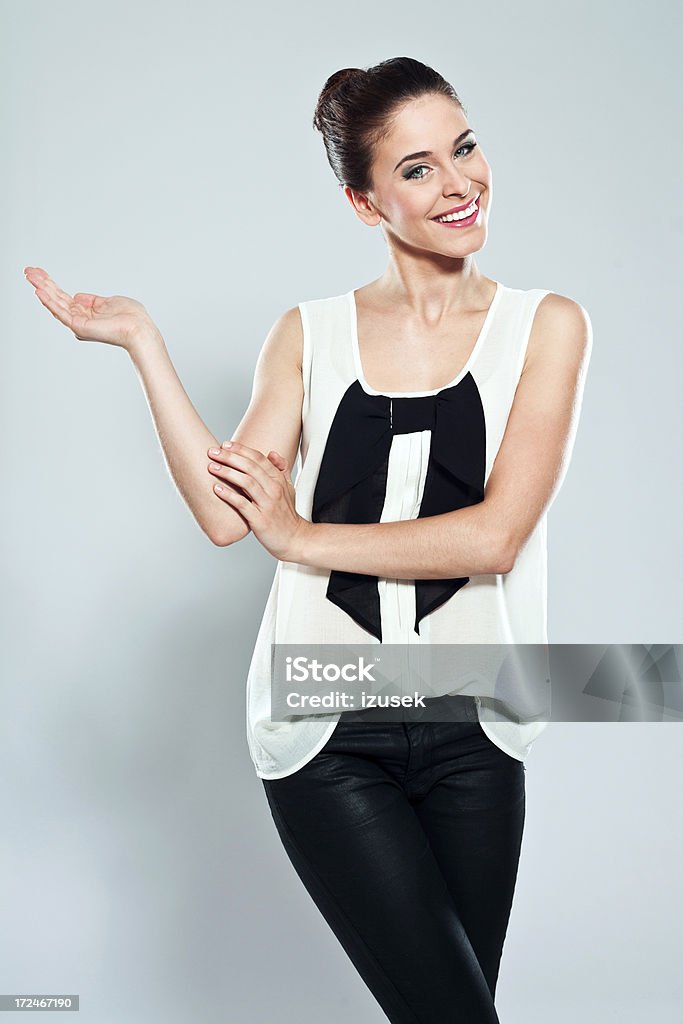 Attractive young woman, Studio Portrait Portrait of attractive young woman pointing at copy space and smiling at camera. Studio shot on a grey background. Fashion Model Stock Photo