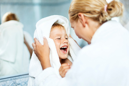 Mother drying up child's hair with a towel in a bathroom after bath.