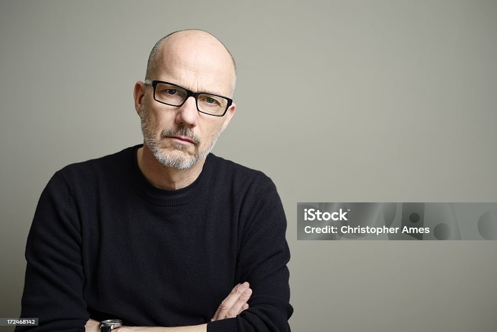 Mature Man Looking at Camera A handsome, balding mature man with glasses, wearing a black t-shirt and cashmere sweater, looks seriously at the camera. Mature Men Stock Photo