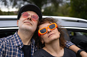 mature couple standing by a car wearing colorful glasses