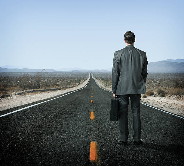 istock Businessman holding briefcase looking down long desert highway 172469240