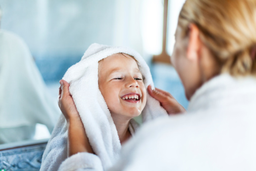 Mother drying up child's hair with a towel in a bathroom after bath.