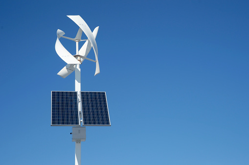 A combined vertical axis wind turbine and solar panel in bright sun with blue sky background.