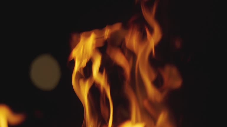 SLOW MOTION, MACRO, DOF: Bright sparkles flying out of a orange campfire burning in the pitch dark. Cinematic shot of orange flames engulfing coals in a campfire and sparks popping up into the air