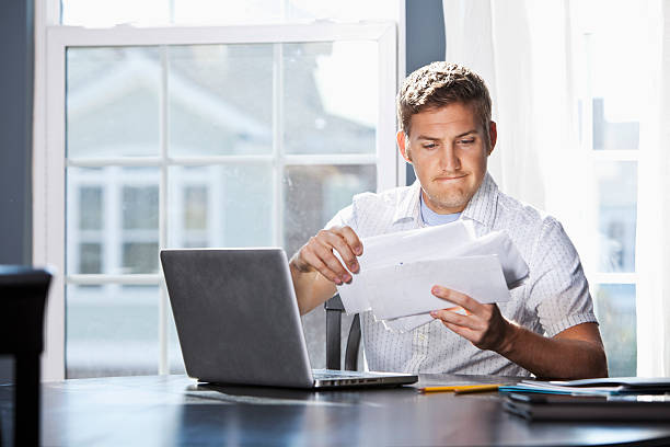 Paying bills Young man (20s) with laptop, going through mail, paying bills. Sc0601 stock pictures, royalty-free photos & images