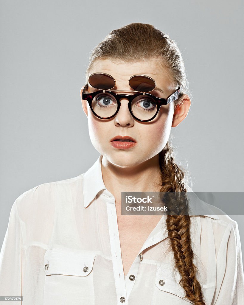 Disbelief Portrait of shocked young adult woman wearing nerd glasses staring at camera. Studio shot on grey background. Anxiety Stock Photo