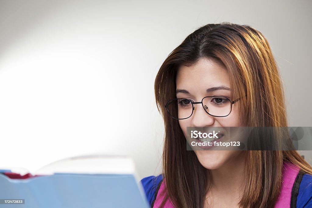 Retrato: Bela adolescente vestindo óculos, sorrindo e lendo livro didático - Foto de stock de 16-17 Anos royalty-free