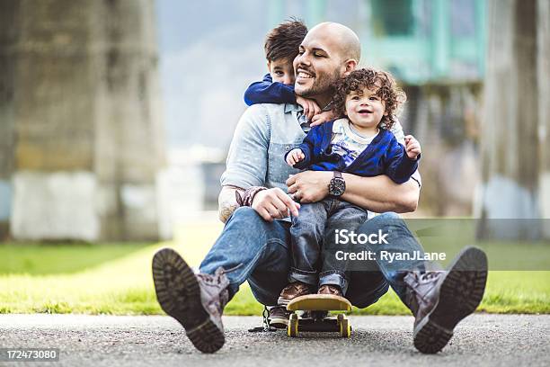 Papà Su Uno Skateboard In Un Parco Con Due Figli - Fotografie stock e altre immagini di Padre - Padre, Famiglia, Etnia latino-americana
