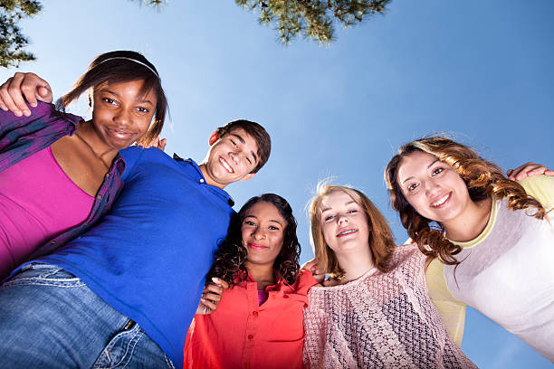 istock Relationships: Teenagers Smiling in a huddle against clear blue sky 172473378