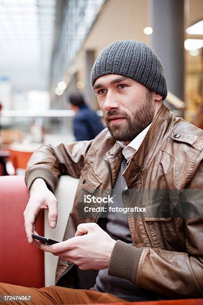 Foto de Homem Bonito Sentado Em Cafe Tem Telefone Celular Nas Mãos e mais fotos de stock de 25-30 Anos