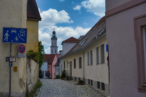 Germany, Freising - May, 2021: Narrow street with traditional old colorful houses with view at St. George church tower in the historic centre of Freising, located near Munich.