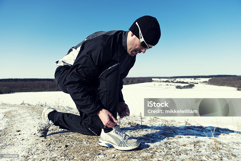 Corridore in inverno paesaggio annodare una scarpa - Foto stock royalty-free di Abbigliamento sportivo