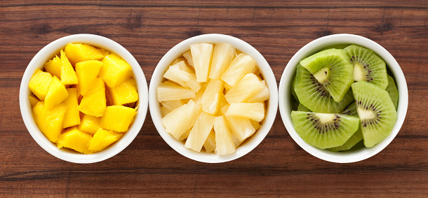 Three bowls containing diced mango, pineapple and kiwi