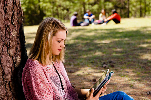 istock Technology: Female teen uses digital tablet under tree. Group behind. 172478001