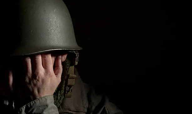 World War Two American soldier suffering from shell shock as he covers his face with his hands. Spotlit studio shot with deep shadows and a black background for a more dramatic image. Plenty of space for type.