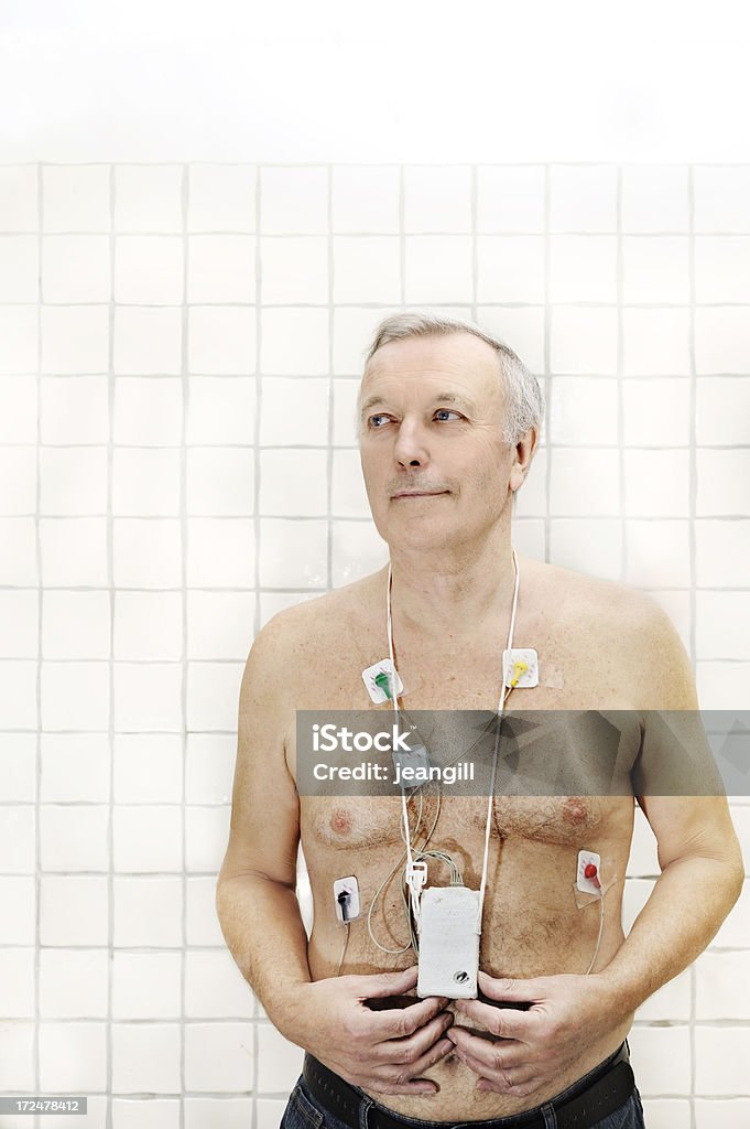 Senior wearing heart monitor "Senior patient wearing a heart monitor, in a cloth case, hung round his neck and attached to five sensors stuck to the chest. This apparatus is designed to be worn for 24hours and monitor heart activity during this period.More like this" 65-69 Years Stock Photo
