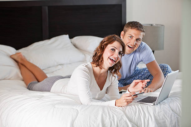 Couple shopping on the internet Young couple (20s) in bedroom, shopping on the internet.  Focus on woman. Sc0601 stock pictures, royalty-free photos & images