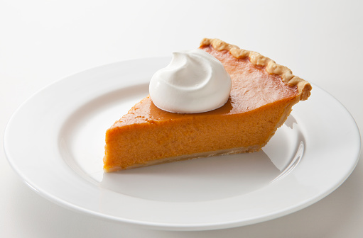 A slice of pumpkin pie with whipped cream on a light background.