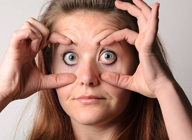 Close up shot of a young woman holding her eyes open with her fingers.
