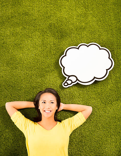Asian girl lying on grass in park or garden looking at copy space with thought bubble ove rher head...thinking or day dreaming