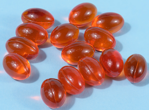 Orange capsules with fish oil on a blue background, top view
