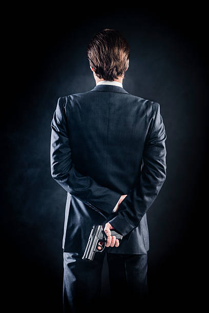 Mafioso, gangster, suit, gun, slicked back hair, rear view, studio The mafioso man in a suit with gun and slicked back hair. Rear view, studio shot, dark background. slicked back hair stock pictures, royalty-free photos & images