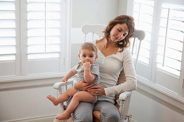 Mother napping with baby in lap Young mother (20s) resting in rocking chair with baby (8 months) sitting on lap. Sc0601 stock pictures, royalty-free photos & images