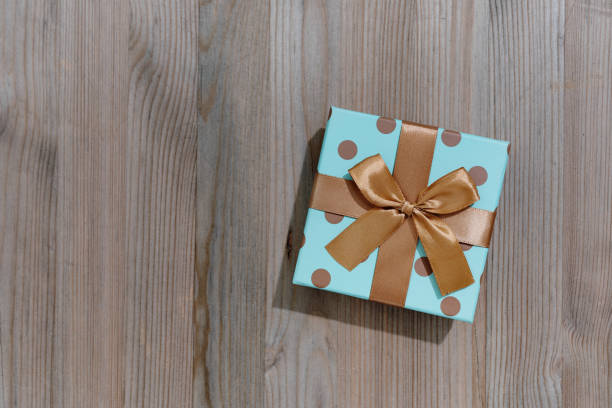 Festive gift box with golden ribbon on wooden background. Square format.