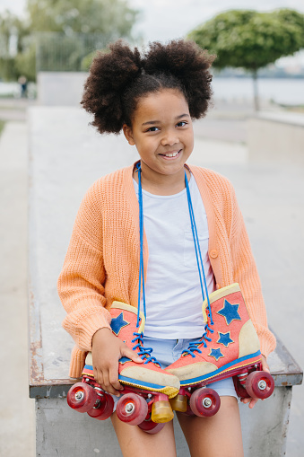 Portrait of a beautiful cheerful girl carrying roller skates having fun in the skate park.