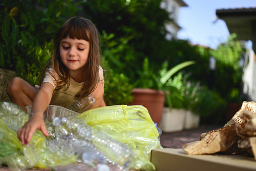 little girl sorting plastic waste in courtyard.