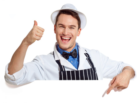 Portrait of a happy male butcher pointing at the white board and laughing at the camera. Studio shot isolated on a white background.