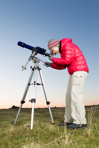 Female amateur astronomer looking through her three inch refracting telescope at sunset in readiness for an evenings skyviewing. AdobeRGB colorspace. More astronomy themes in this lightbox::