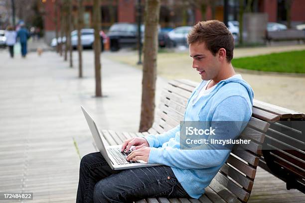 Atractiva Joven Hombre Utiliza Un Ordenador Portátil En Un Parque De Banco Foto de stock y más banco de imágenes de Adulto joven