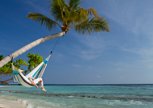 A young man is having a nap in a hammock over the sea.