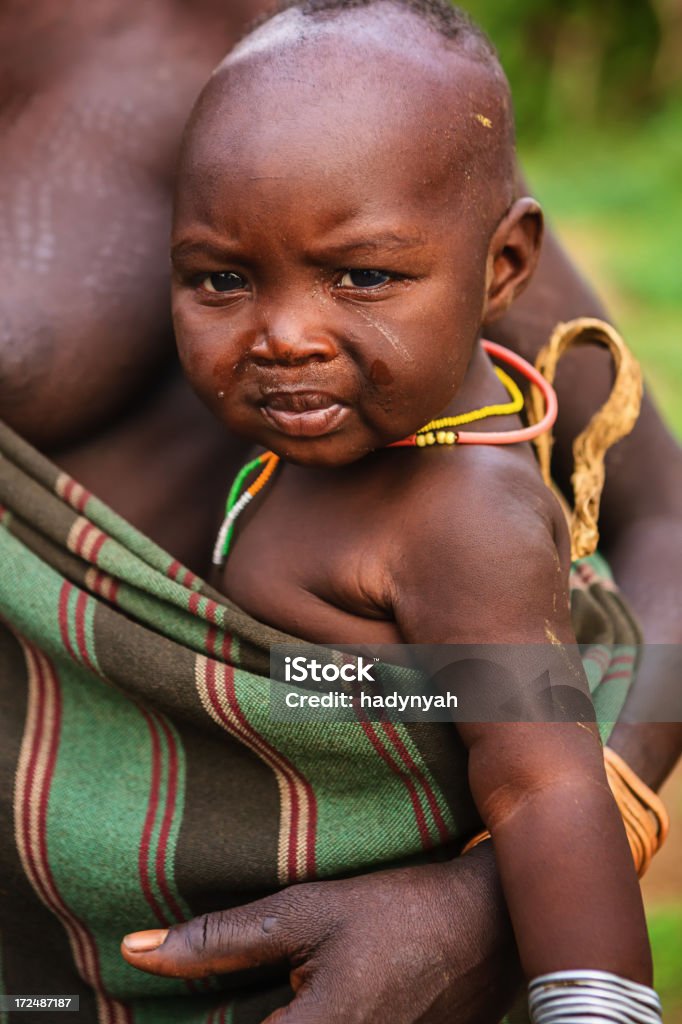 Portrait of woman from Mursi tribe, Ethiopia, Africa Woman from Mursi tribe holding her baby.  Mursi tribe are probably the last groups in Africa amongst whom it is still the norm for women to wear large pottery or wooden discs or aEplatesaa in their lower lips. Adult Stock Photo