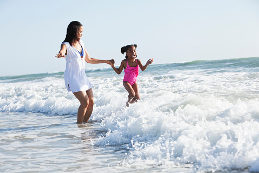 African American mother (30s) and daughter (6 years) at the beach, playing in the surf.