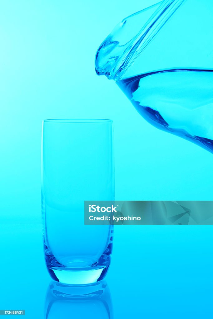 Blue tinted image of pouring water into a glass Blue tinted image of pouring a fresh water into a glass against blue background. Activity Stock Photo
