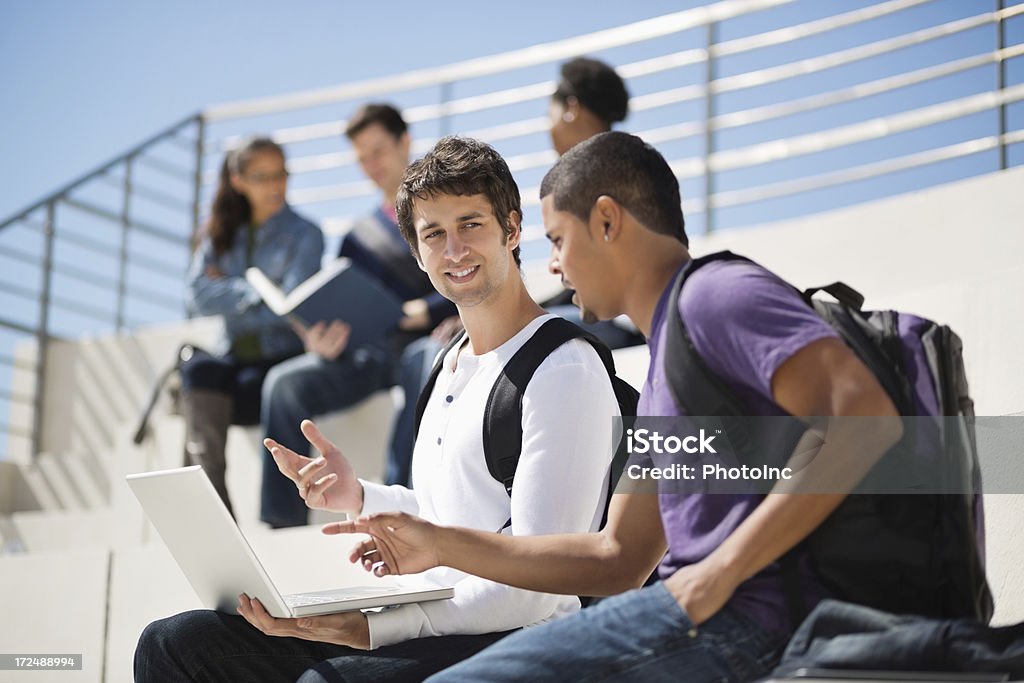 Hombre con ordenador portátil hablando de estudiantes en el Campus - Foto de stock de 18-19 años libre de derechos
