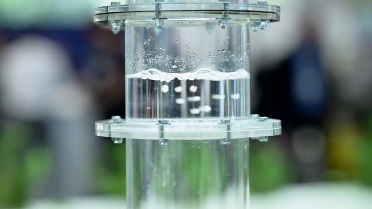 Hydrogen gas bubbeling through a membrane in a plastic cylinder filled with water, small bubbles forming in liquid, slow motion, zoom out