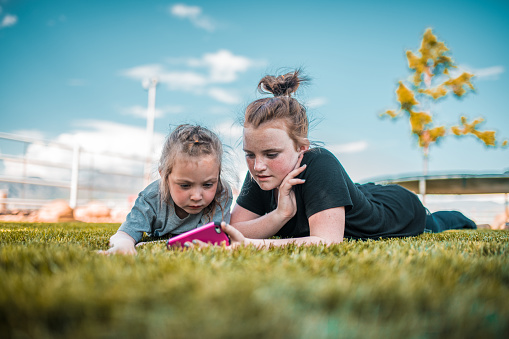 Young girls lying on the grass using a smartphone.
