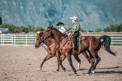 Young Cowboys and cowgirls riding a horse in a rodeo arena. About to barrel race.