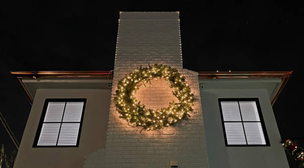 Large wreath with lights on a side of a white house at night.  Wreath lights illuminated.