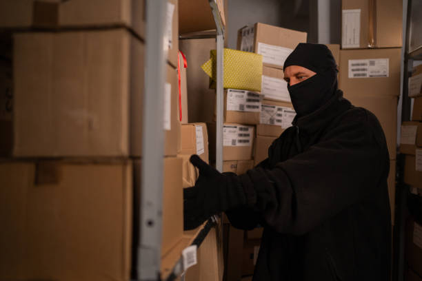 istock Thief in black gloves take a boxes of goods in a warehouse at night. Security problems in warehouses and stores. 1725057697